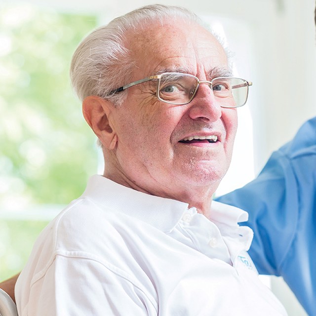 Older man smiling, with a carer at his side